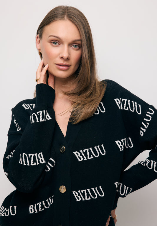 Modelka z ręką przy twarzy ubrana w czarny, logowany kardigan KYLE.