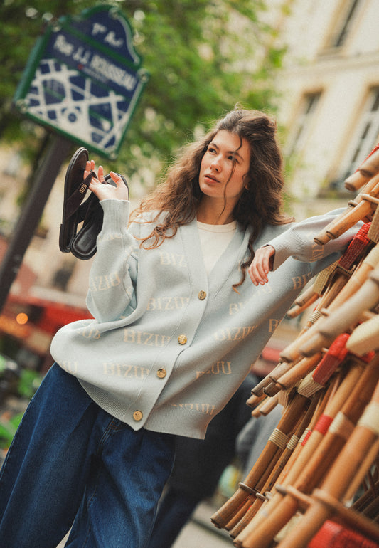 Modelka z jedną ręką w kieszeni spodni ATLANTA, ubrana w błękitny sweter KYLE w logo.