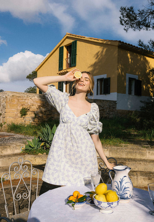 Modelka stoi w ogrodzie z cytryną przy oku z jedną ręką opartą na krześle. Ubrana w mini sukienkę ALMAR.