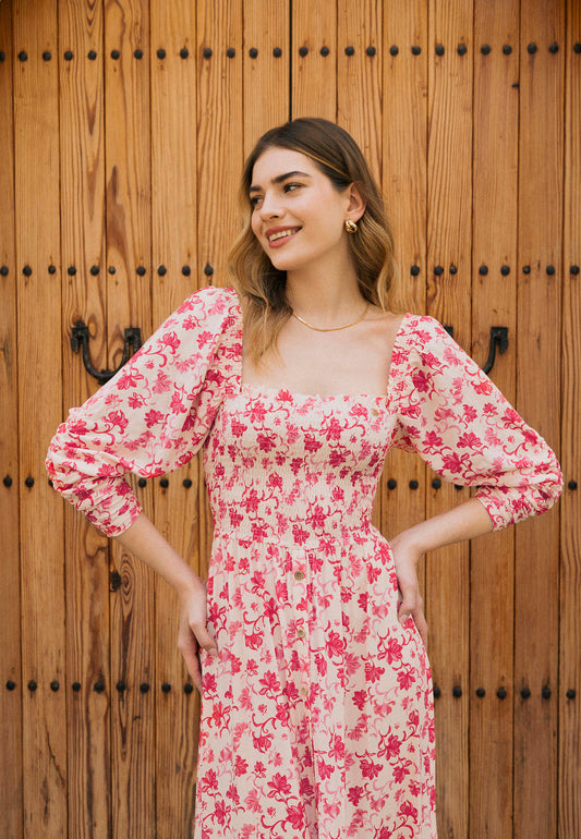 Zbliżenie na modelkę stojącą na tle drewnianych drzwi z rękoma na biodrach w kwiatowej sukience PATRYA.