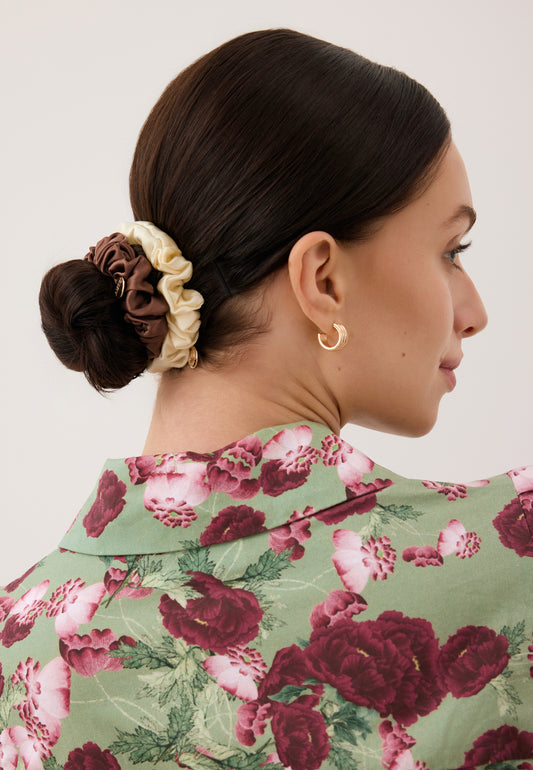 Zbliżenie na włosy modelki związane w ciasny kok jedwabnymi gumkami ALLY w kolorze brązowym i kremowym.