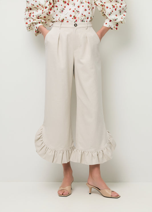 Zbliżenie na nogi modelki w bezowych spodniach NELLA z ozdobnymi falbankami na dole.