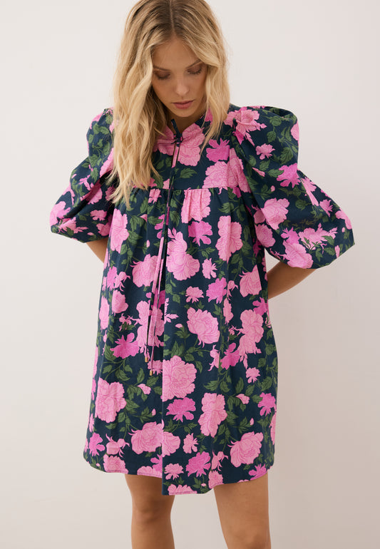 Zbliżenie na modelkę z rękoma trzymanymi z tyłu, ubrana w mini sukienkę w kwiatowy print AYOTE.