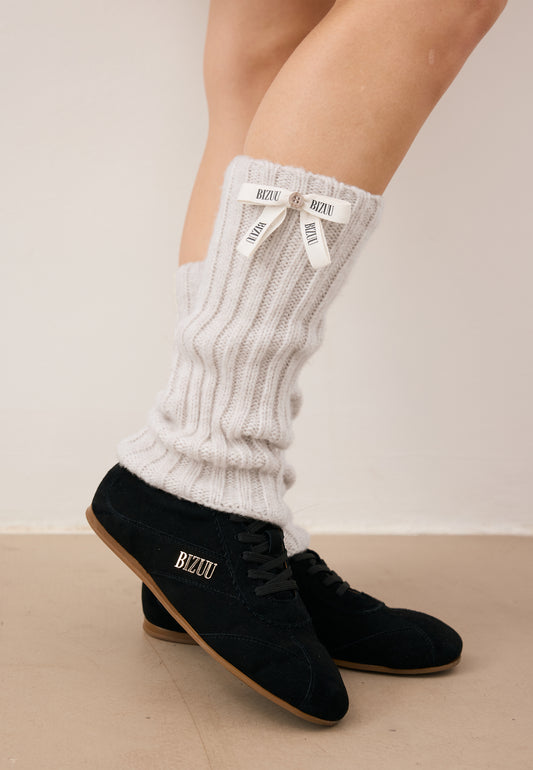 Zbliżenie na nogi modelki gdzie jedną stopę trzyma opartą na palcach. Na nogach ma założone beżowe getry CHAFI oraz buty LEOLA.