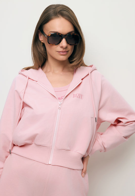 Zbliżenie na modelkę w rozpinanej różowej bluzie dresowej CIANA oraz w okularach przeciwsłonecznych VILLALTA.