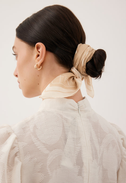Zbliżenie na włosy modelki ciasno upięte w kok, na którym zaplątana jest apaszka beżowa ARIA z jedwabiu.