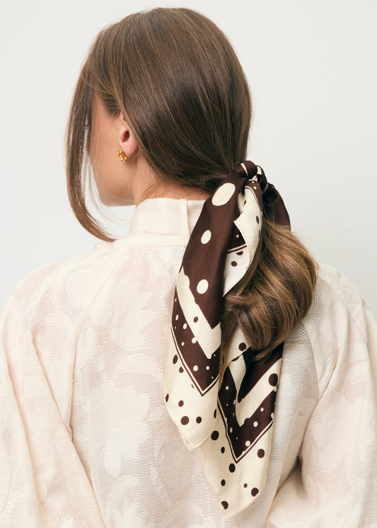Zbliżenie na włosy modelki przewiązane brązową jedwabną apaszką w kropki DOTTI.