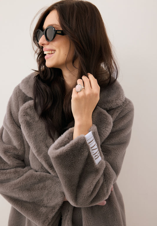 Zbliżenie na modelkę w czarnych okularach przeciwsłonecznych ENNA oraz futrze LIVORNO w kolorze taupe.