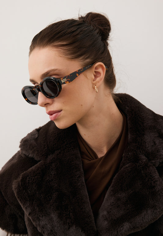 Zbliżenie na modelkę w brązowych okularach ENNA oraz w brązowym futrze.