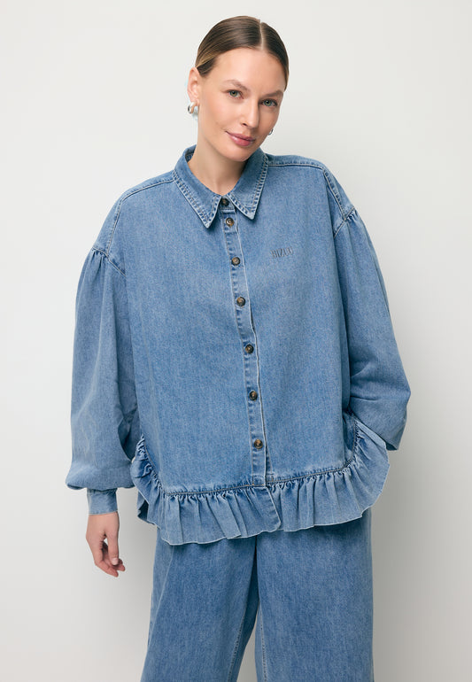 Modelka z ręką w kieszeni spodni jeansowych NELLA, do kompletu ubraną ma koszulę z falbaną na dole FALBI.