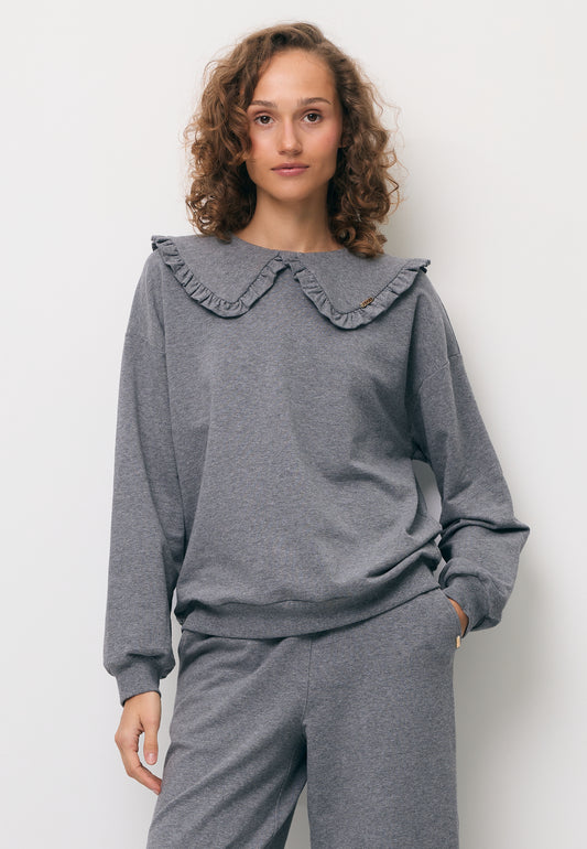 Modelka z jedną ręką w kieszeni spodni BAYLE. Ubrana w szarą luźną bluzę z ozdobnym kołnierzem FALLS.