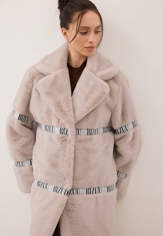 Modelka spoglądająca w dół ubrana w beżowe futerko FLORENCE z logowaną taśmą.