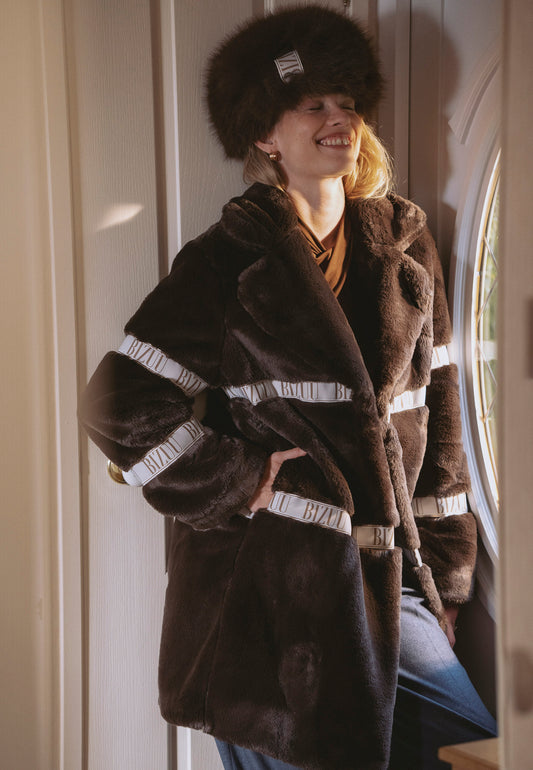 Uśmiechnięta modelka ubrana w brązowe futro FLORENCE z lampasami.