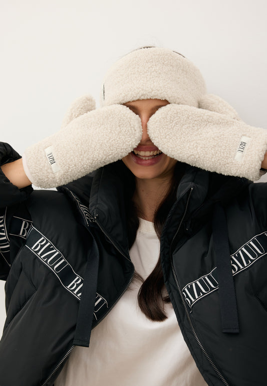 Modelka zasłaniająca oczy kremowymi rękawiczkami SNUGGIE z imitacji kożuszka.