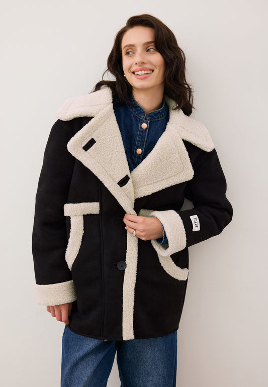 Uśmiechnięta modelka zapinająca guzik kożuszka LAFARA w kolorze czarnym z ozdobnym logo na rękawie.