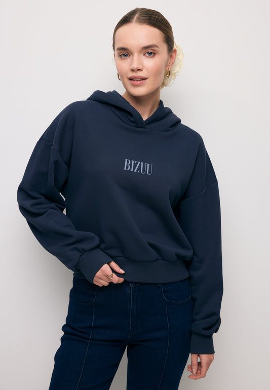 Zbliżenie na modelkę w granatowej bluzie z kapturem i niebieskim logo na przodzie SAY.