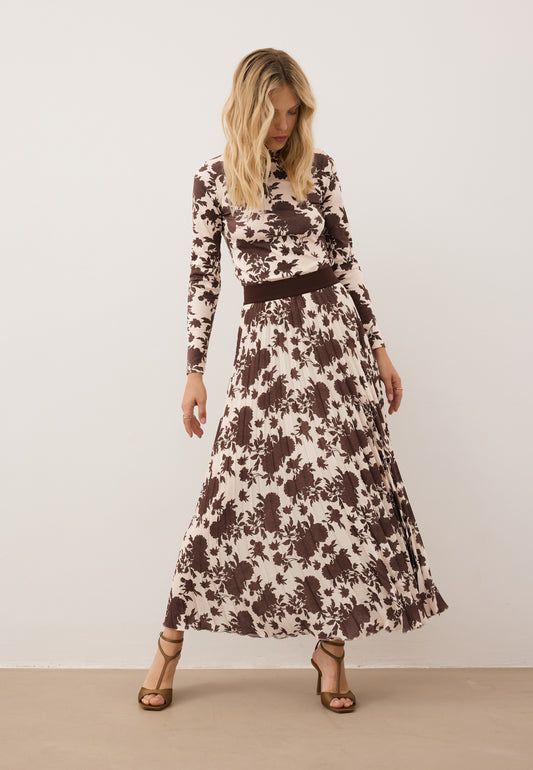 Modelka kołysząca się na boki, spoglądająca w dół. Ubrana w obcisły golf OWAKA oraz plisowaną spódnicę maxi MINA