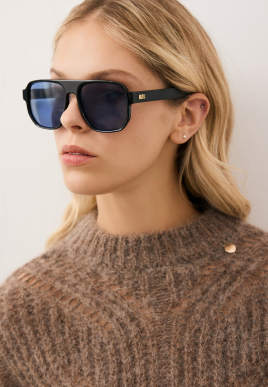 Zbliżenie na modelkę w czarnych okularach z niebieską soczewką MISTRETTA.