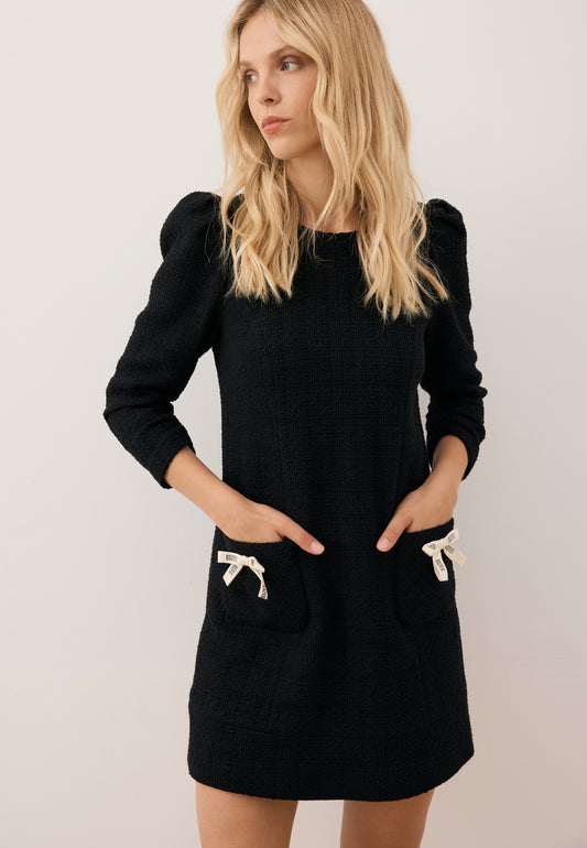 Modelka z rękoma w kieszeniach sukienki NOILLY, kieszenie ozdobione logowanymi kokardkami.