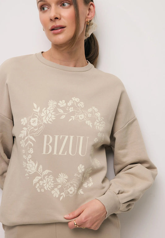 Zbliżenie na modelkę w beżowej bluzie ORISA z ozdobnym nadrukiem w kształcie wieńca.