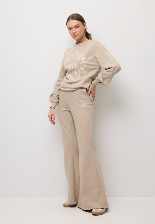 Modelka w beżowych spodniach z szerokimi nogawkami ZEIA oraz bluzę z logo ORISA.