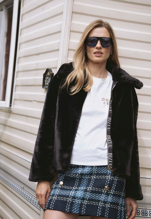 Modelka oparta o przyczepę campingową ubrana w krótkie futerko PIACENZA i spódniczkę DISSA.