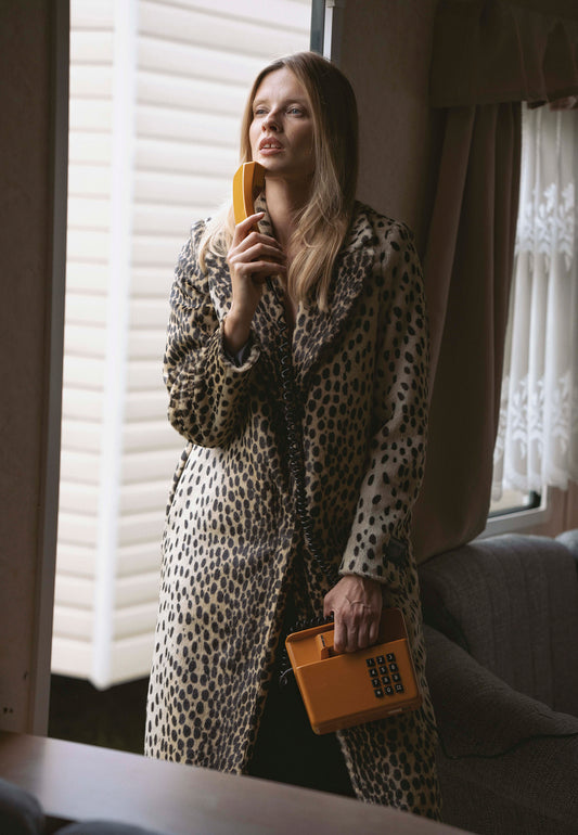 Modelka stojąca przy oknie trzymająca w ręce telefon stacjonarny. Ubrana w płaszcz futrzany w zwierzęcy print PONTICLLI.