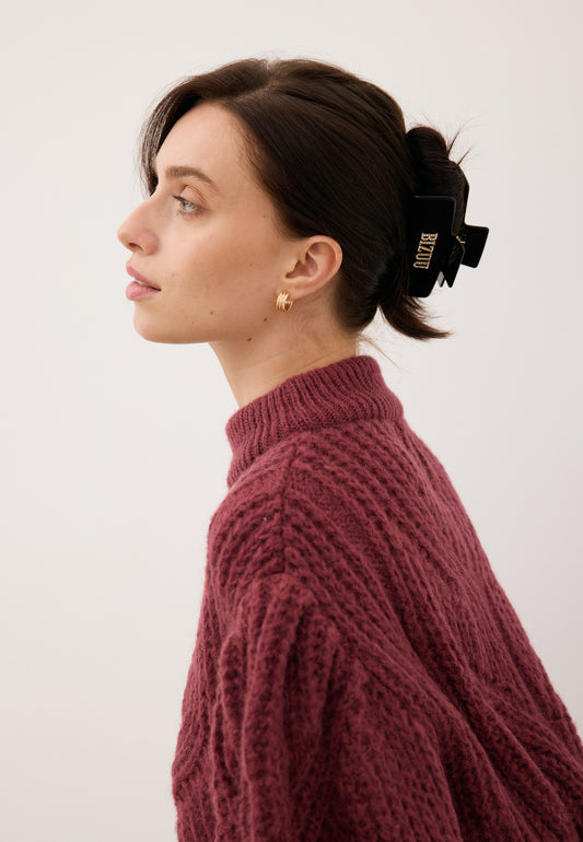 Modelka stojąca bokiem z włosami upiętymi czarną, prostokątną klamrą RHODI z logo z cyrkonii.