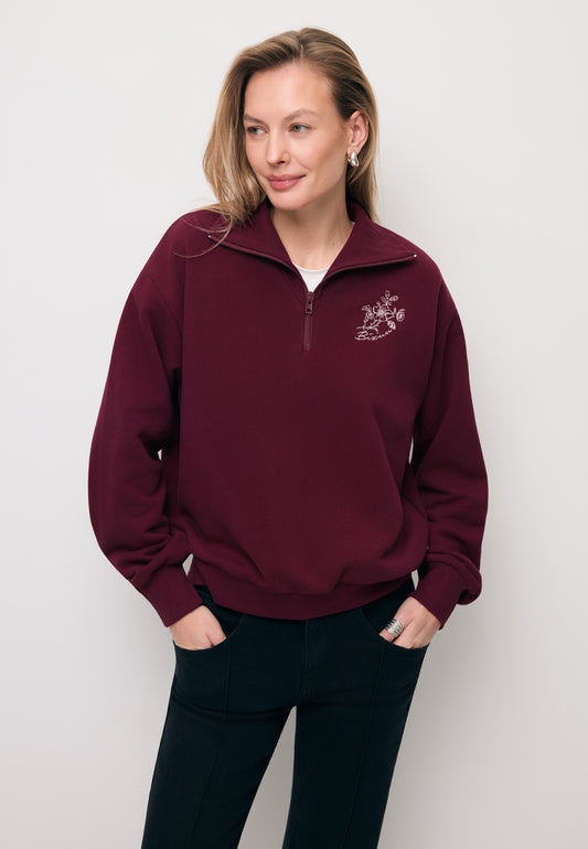 Modelka z rękoma w kieszeni spodni ubrana w bordową bluzę typu half-zip TANSY.