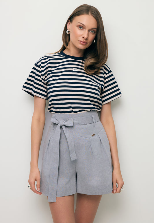 Zbliżenie na modelkę w T-shircie w biało-granatowe paski TISHALLY oraz szarych spodenkach z wysokim stanem KANDYS.