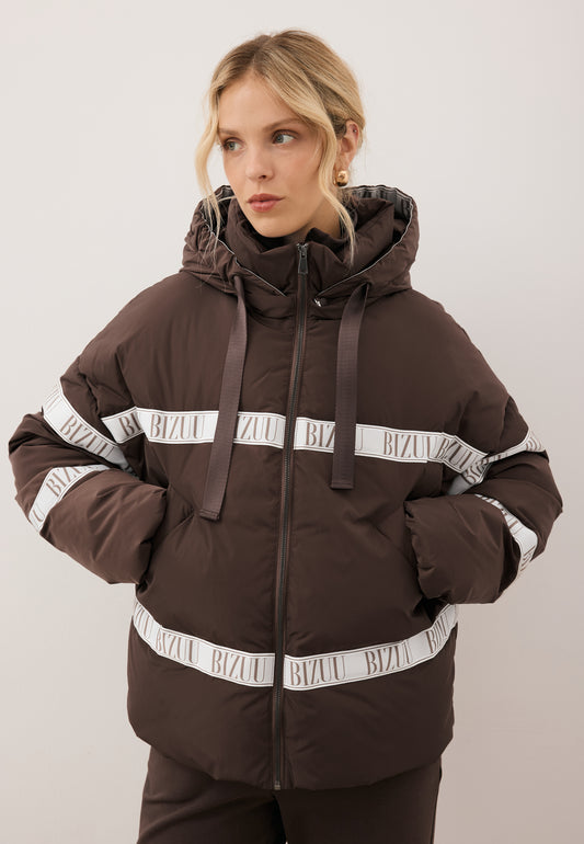 Zbliżenie na modelkę z rękoma w kieszeni brązowej kurtki TOKYO z naturalnym wypełnieniem oraz logo.