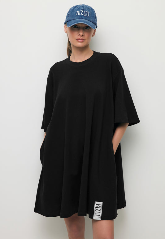 Zbliżenie na modelkę w mini dzianinowej sukience TRESS ozdobną logowaną metką oraz niebieską czapką z daszkiem ZANE.