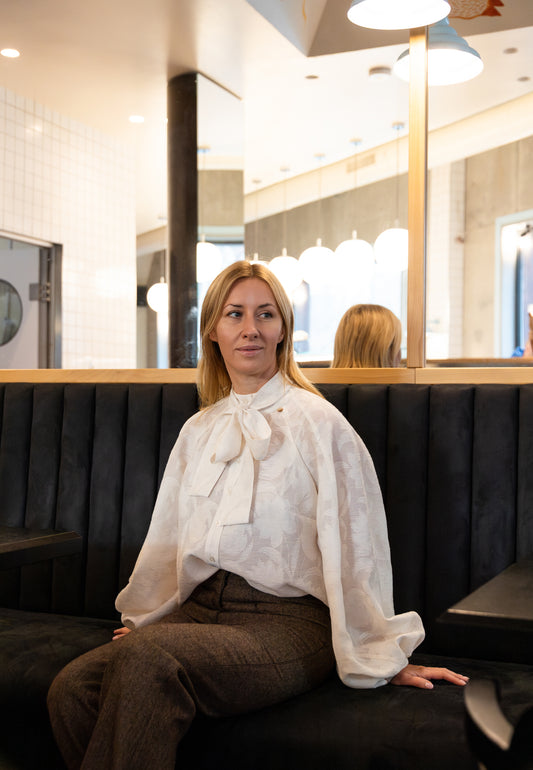 Modelka siedząca na kanapie w restauracji ubrana w kremową koszulkę VALEA w kwiatowy wzór.