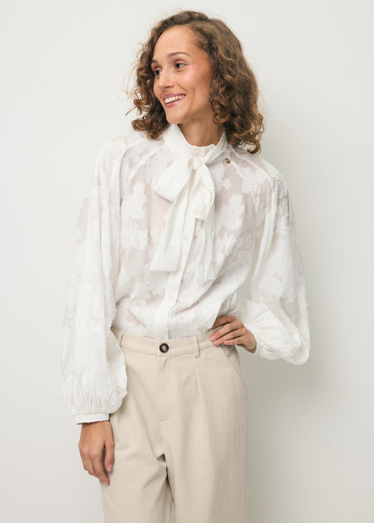 Uśmiechnięta modelka ubrana w koszulę z ozdobną kokardą pod szyją VALEA.