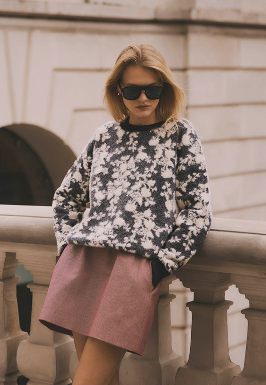 Modelka oparta o murek ubrana w sweter CANELA w kwiatowy wzór i w bordową mini spódniczkę BREDA.