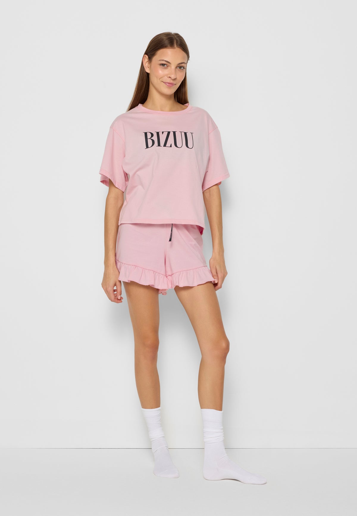 Modelka ubrana w różową piżamę z krótkimi nogawkami i rękawem. Na T-shircie czarne logo Bizuu.