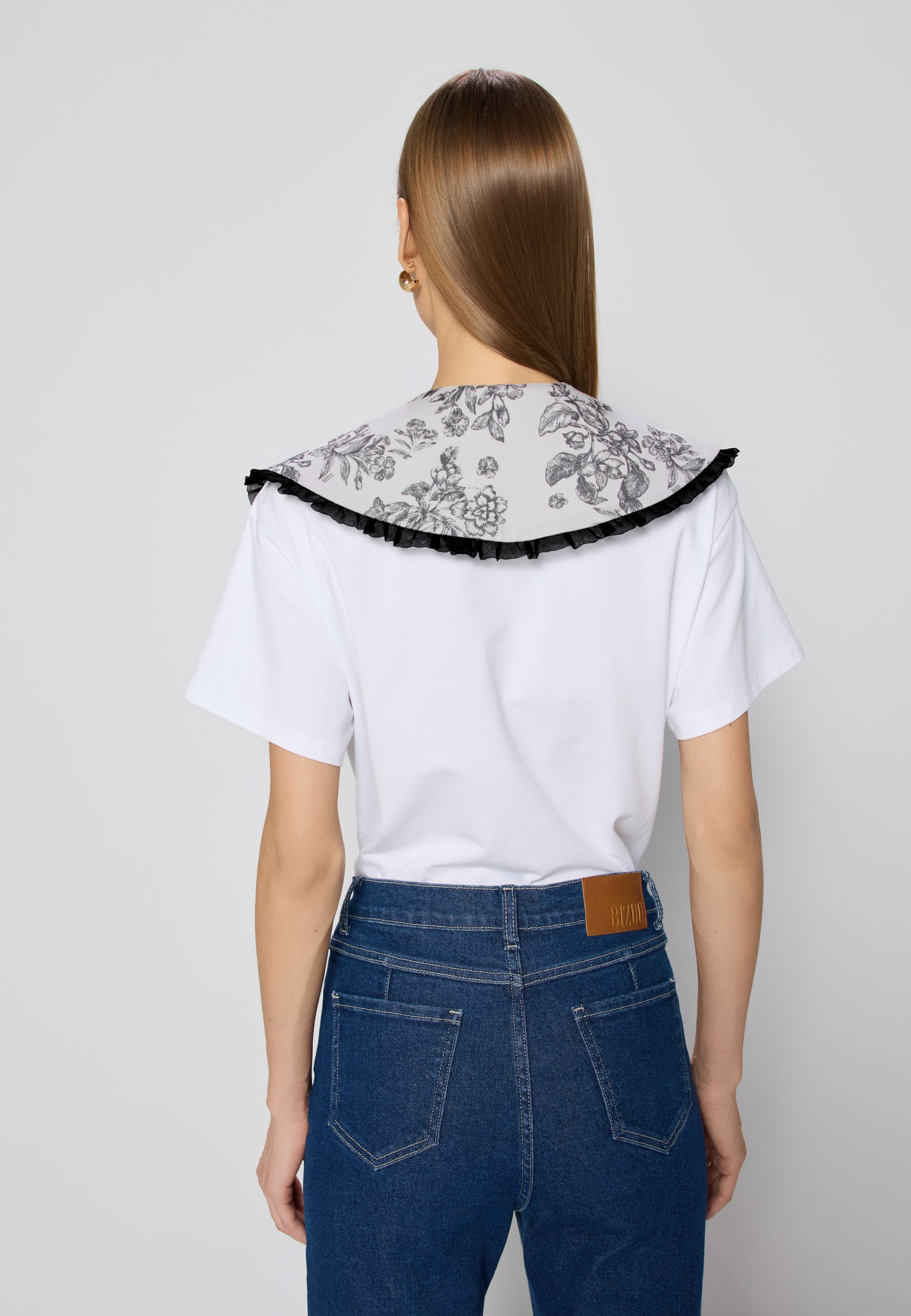 Tylny widok osoby w niebieskich jeansowych spodniach dzwonach i białym t-shircie z kołnierzem w kwiaty.