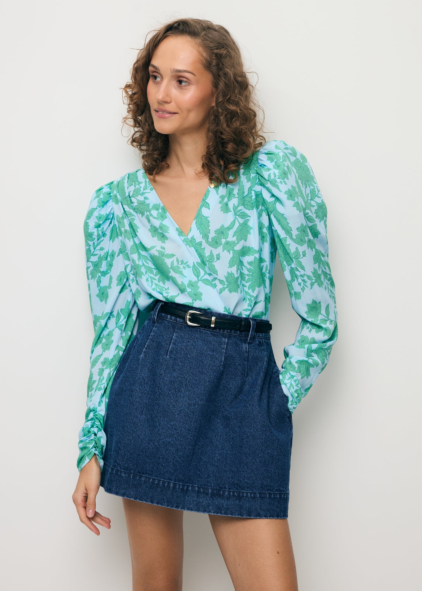 Modelka z ręką w kieszeni denimowej spódniczki BEDA ubrana w kopertowe body ALIBA.