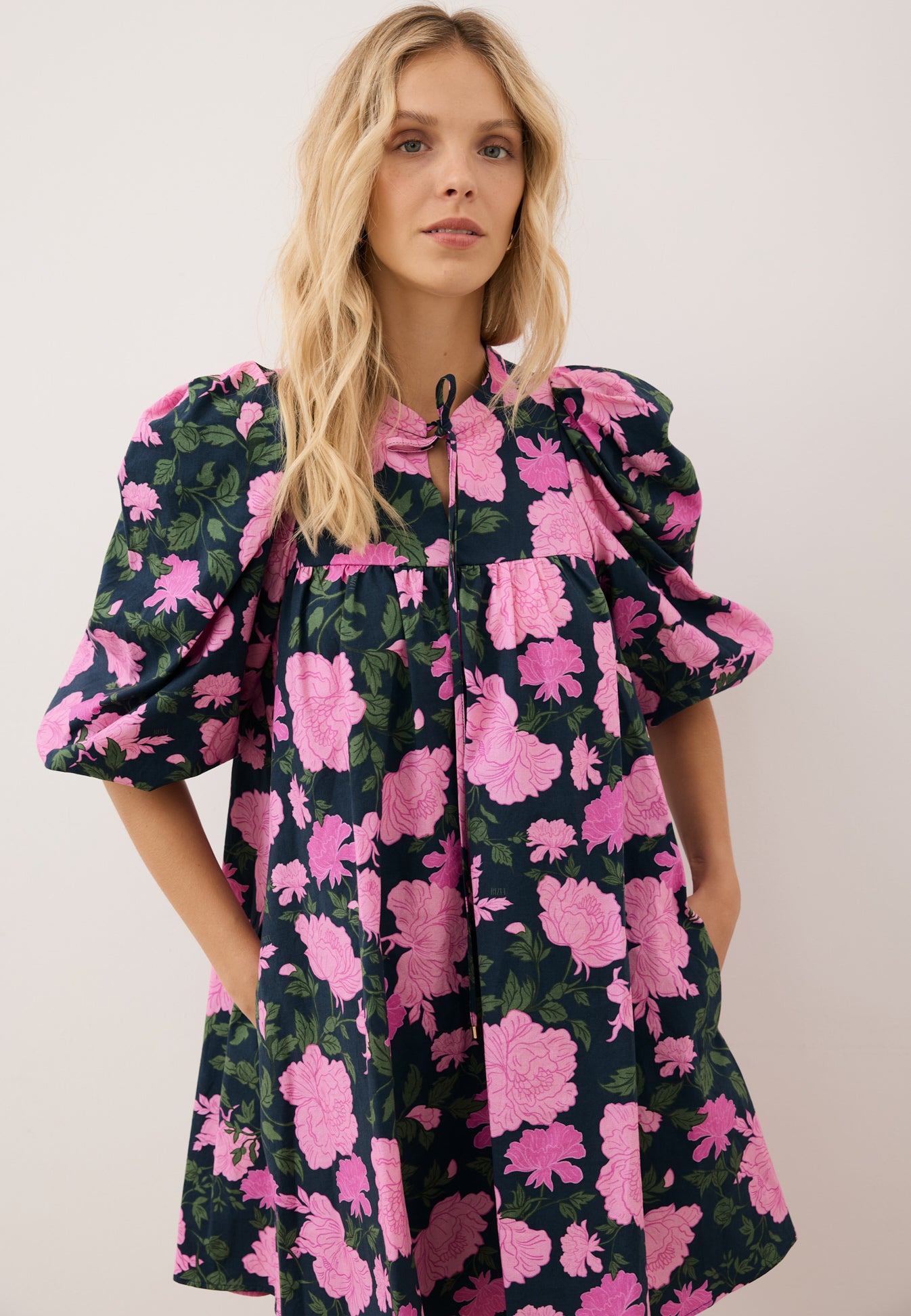 Zbliżenie na modelkę z rękoma trzymanymi z tyłu, ubrana w mini sukienkę w kwiatowy print AYOTE.