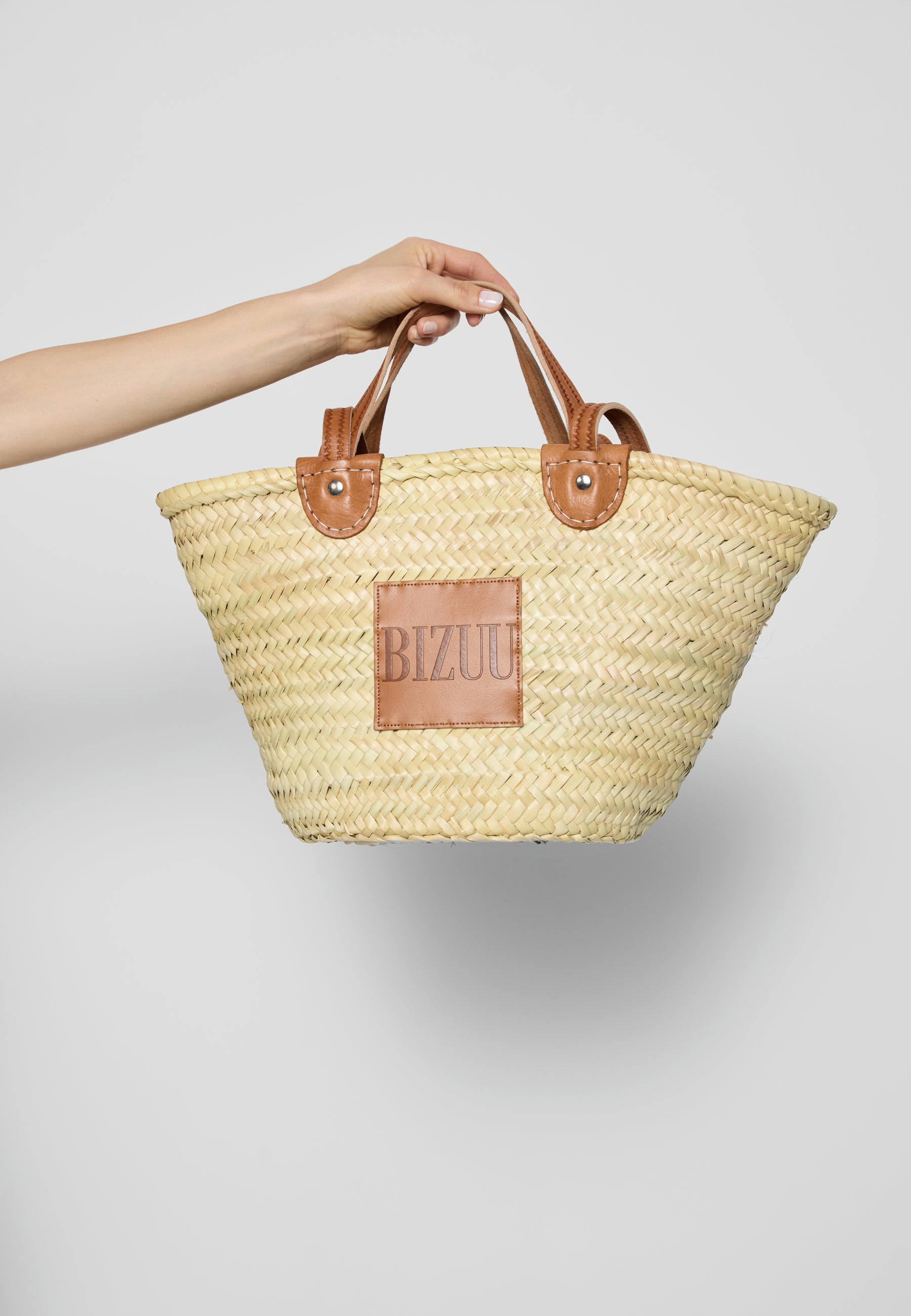 Ręka trzymająca w powietrzu koszyk BASKET za krótkie, skórzane rączki.