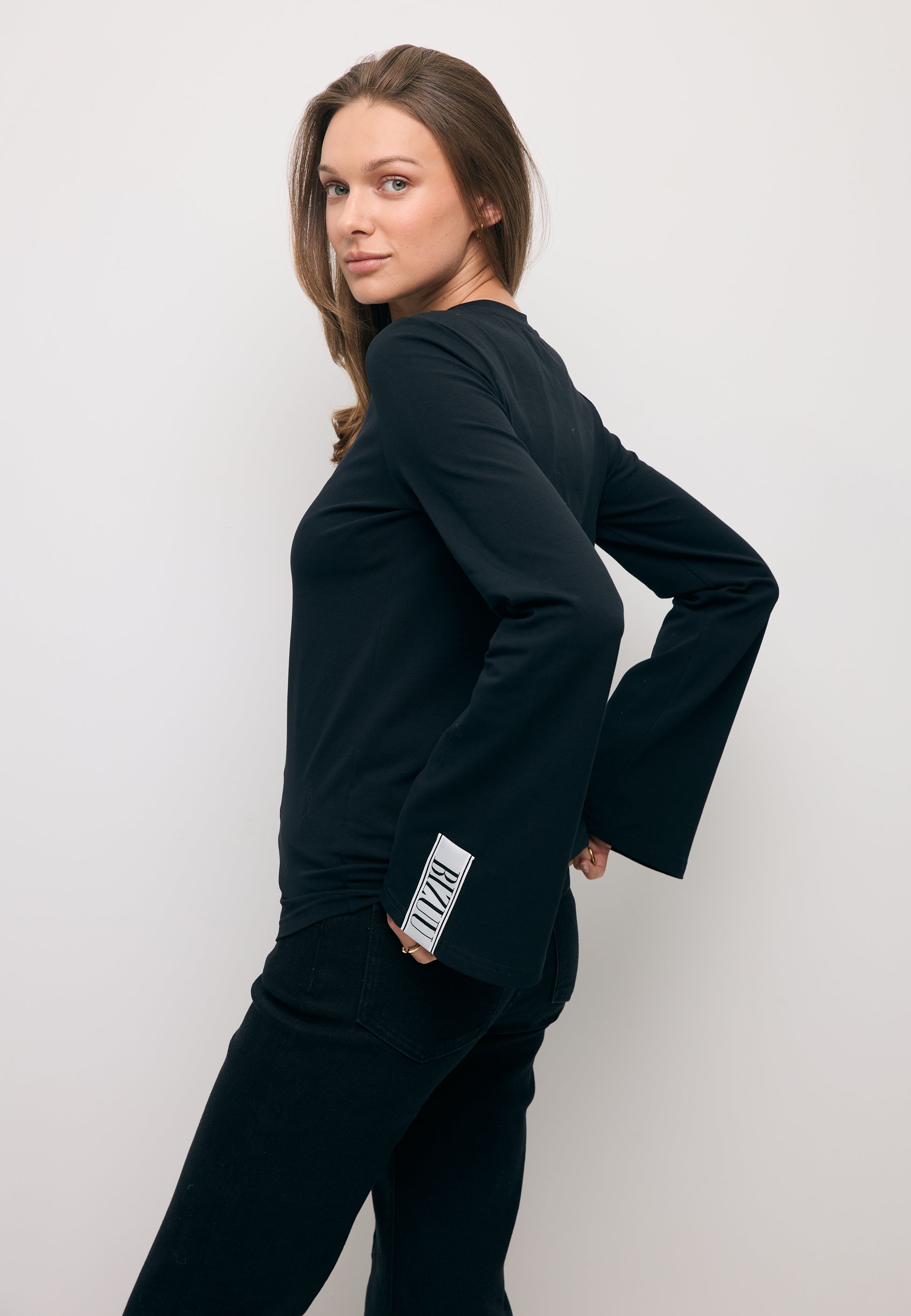 Modelka stojąca bokiem z rękoma w tylnych kieszeniach prezentując szerokie rękawy w longsleeve BELUNNA.