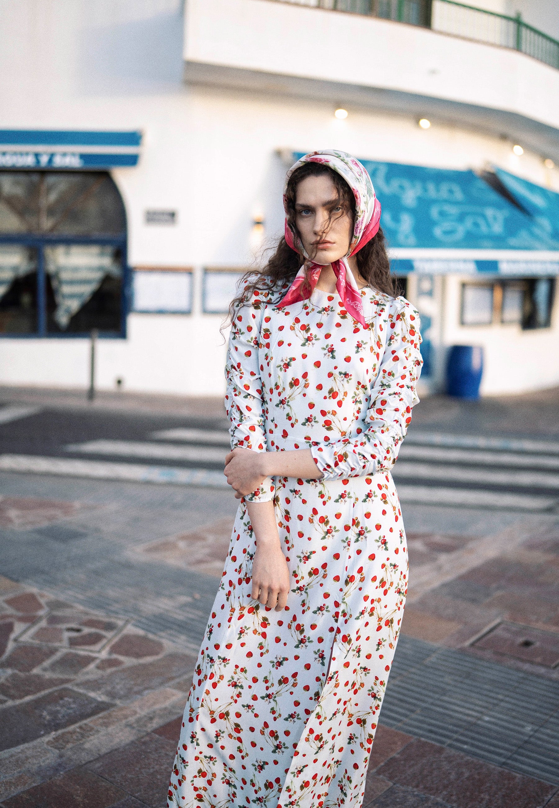 Modelka stojąca na ulicy ubrana w błękitną sukienkę w print z poziomkami CALANA.