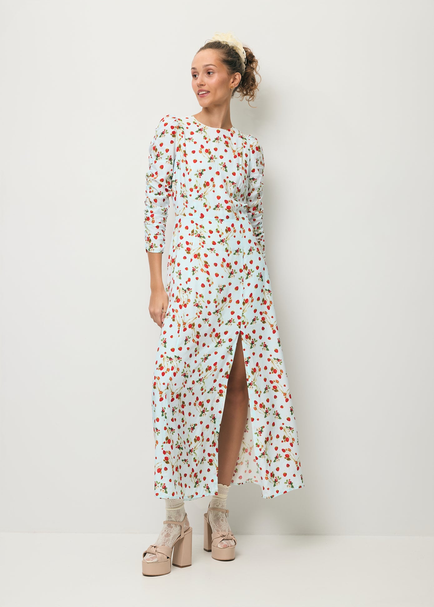 Modelka ubrana w sukienkę midi w print z poziomkami CALANA oraz z rozcięciem na nogę.