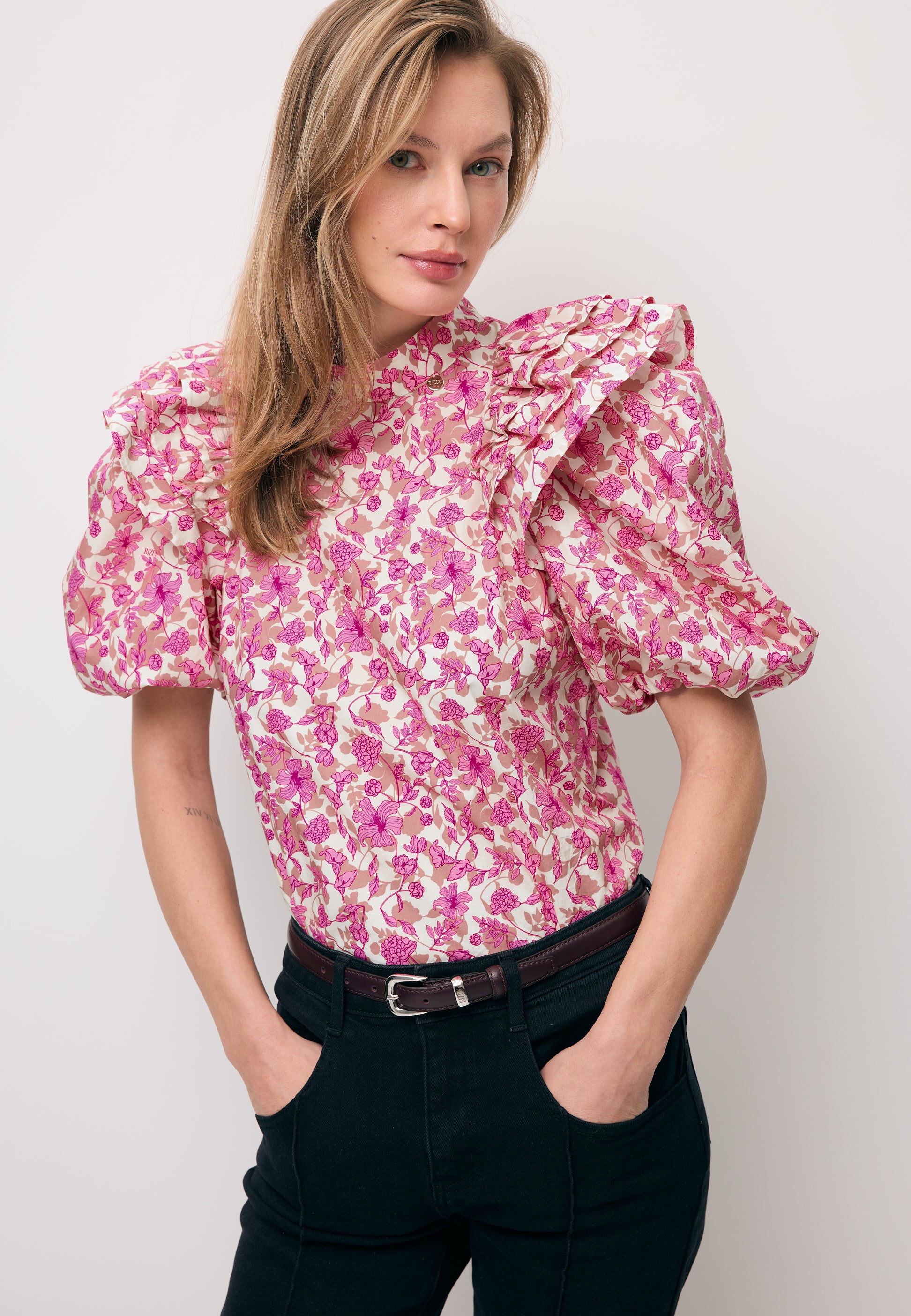 Modelka z rękoma w kieszeni czarnych spodni BELINNA ubrana w bluzkę z bufiastymi rękawami CASSANDRA.