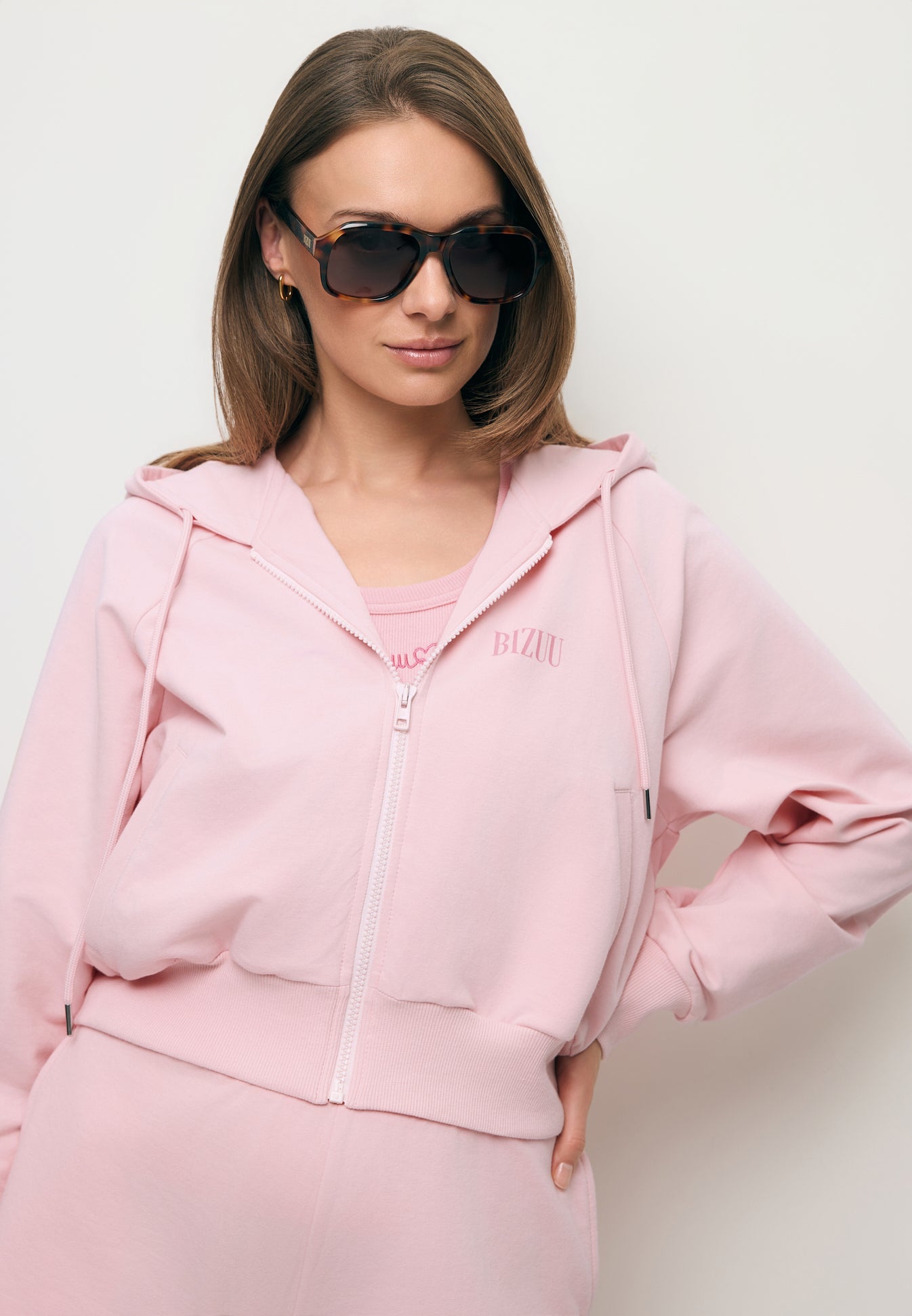 Zbliżenie na modelkę w rozpinanej różowej bluzie dresowej CIANA oraz w okularach przeciwsłonecznych VILLALTA.