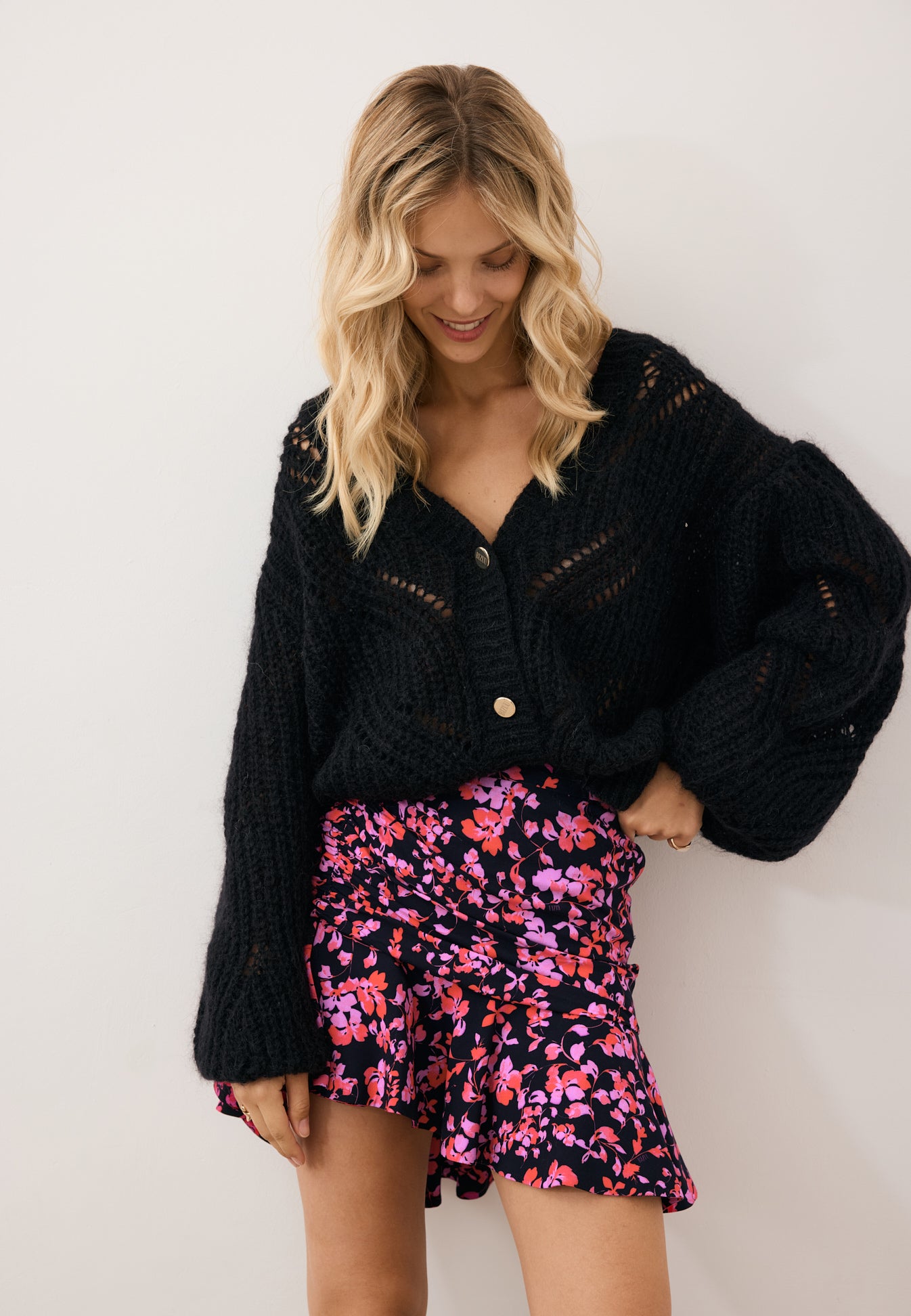 Modelka patrząca w dół w czarnym kardiganie z ażurowym splotem CLARA oraz spódniczkę w kwiatowy print MEXICANA.