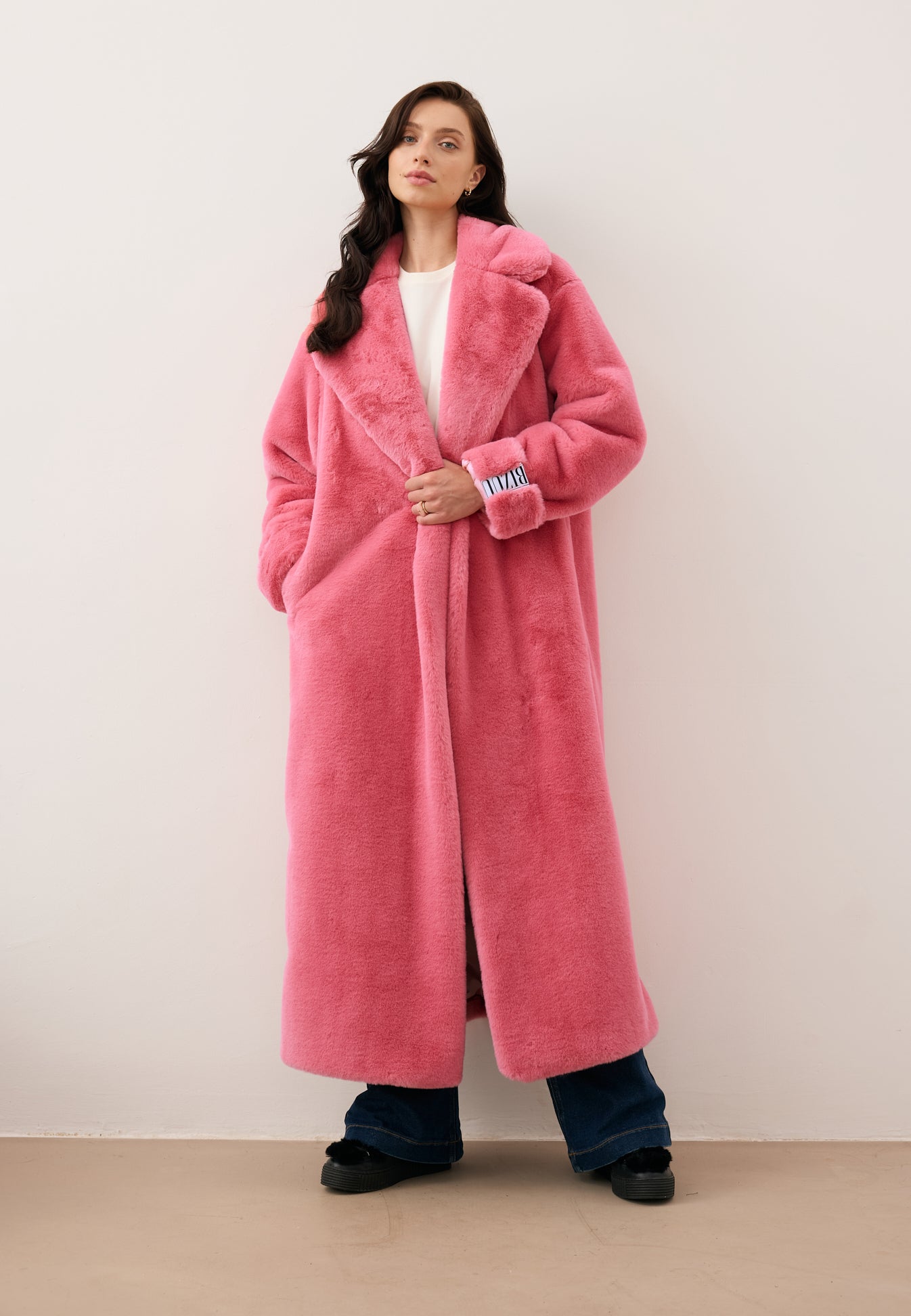 Modelka z jedną ugiętą ręką trzymającą płaszcz futrzany w kolorze różowym DOLOMITES.