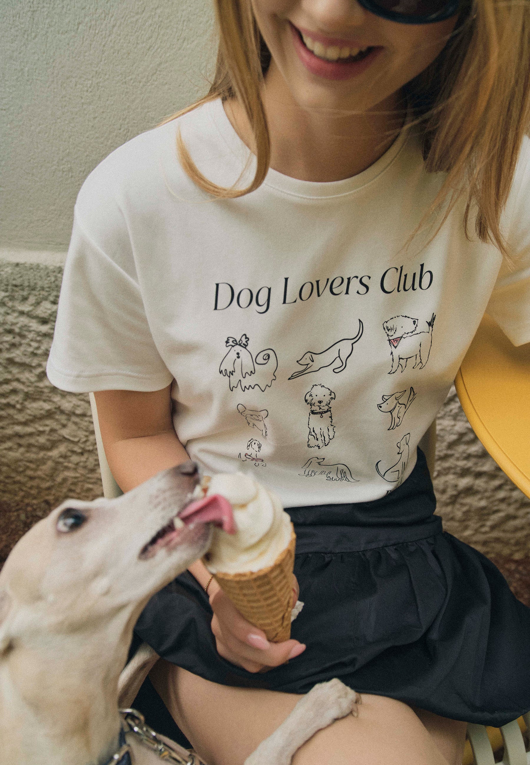 Zbliżenie na modelkę w T-shircie z rysunkami psów i napisem Dog Lovers Club. Modelka trzyma loda, którego liże pies.