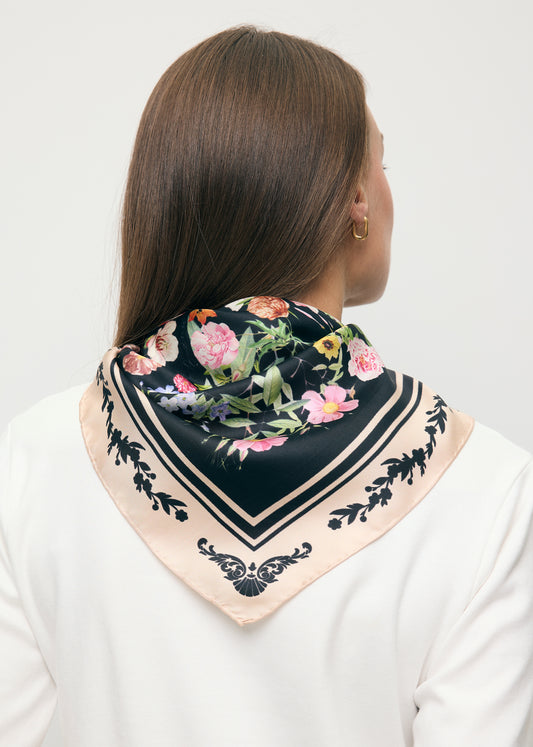 Modelka stojąca tyłem z czarną apaszką z jedwabiu FIORIA na ramionach.