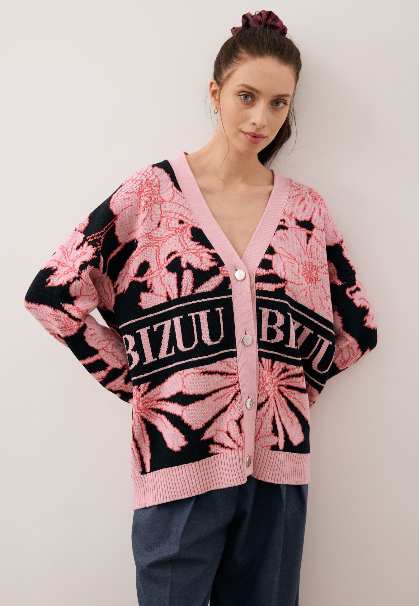 Modelka z rękoma za plecami, patrząca na wprost ubrana w różowo czarny kardigan z logowanymi guzikami HYLES.